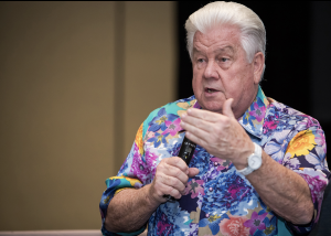 Richard Flint speaking and holding a microphone wearing a colorful shirt